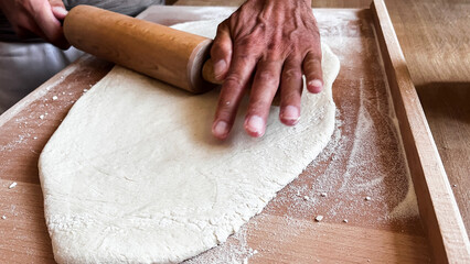 Close up of man's hands rolling dough on wooden table with wooden rolling pin. Homemade baking,...