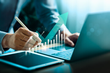 Business growth and financial success concept with rising graph and futuristic analytics. Businessman using digital pen and tablet for data-driven strategy, smart investment, and performance planning.