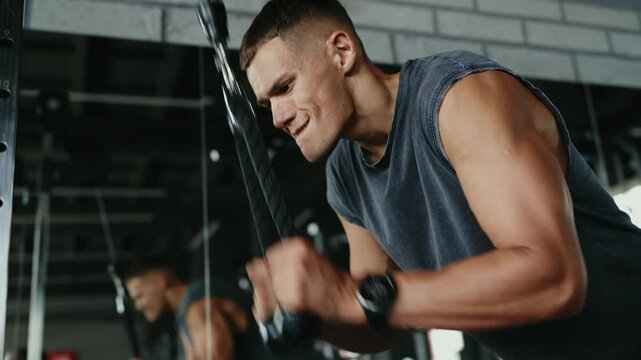 Close-up of a man intensely working out with a tricep rope pulldown at a modern gym, showcasing strength and determination. Focused Man Performing Tricep Rope Pulldown Exercise at Modern Gym