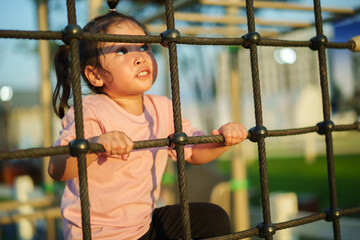 happy toddler girl playing with climbing ropes net at a outdoor playground in park