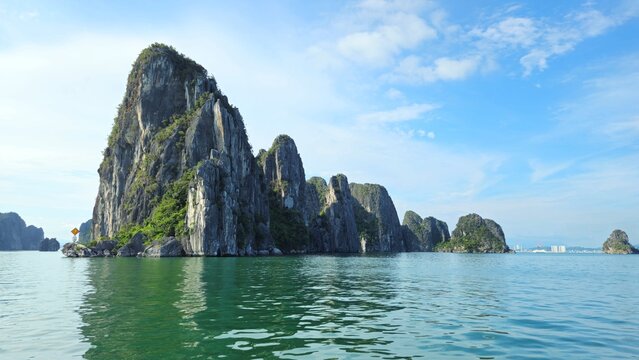Towering limestone islands rise dramatically from the emerald waters of Ha Long Bay, Vietnam, under a bright blue sky. - Powered by Adobe