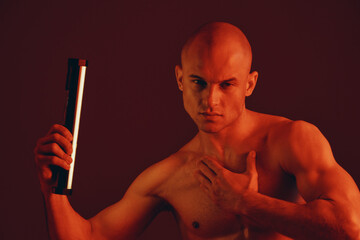 Strong man holding a flashlight, showcasing muscular physique against a dark red background. This...