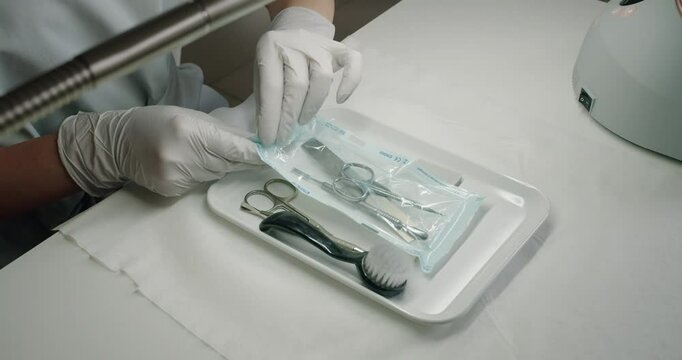 Closeup on master manicure hands in glove opening kraft package with clean sterile instruments for nails treatment procedures in beauty salon.