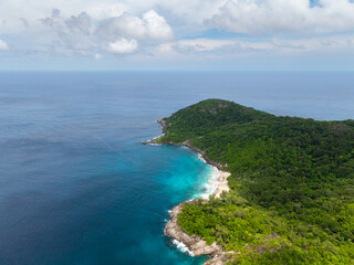 The beach's golden sands are framed by the vibrant, green foliage of the surrounding rainforest. Seychelles, Mahe. Anse Capucins beach.
