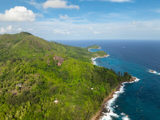 Fototapeta premium Aerial view of rocky shore is washed by the ocean surf and surrounded by tropical vegetation. Seychelles, Mahe.