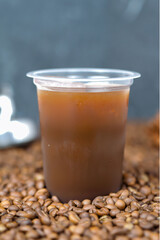 A refreshing iced black coffee served in a clear plastic cup, placed on a bed of roasted coffee beans. The condensation on the cup highlights its cold and fresh taste. 