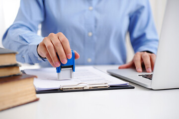 Person stamping document at desk with laptop