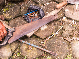 A rusty handsaw, hammer, and nails on a stone floor. Traditional carpentry tools suggest manual labor and rural craftsmanship in a rustic setting.