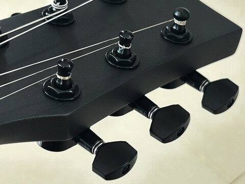 A focused shot captures the sleek black headstock of an Enya Nova Go Sonic guitar, highlighting its tuning pegs and the smooth lines of its design.