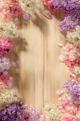 Floral frame on wooden surface with pink, purple, and white blooms and petals for a fresh spring vibe.