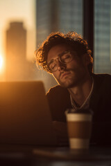 Exhausted professional taking a nap at his desk, golden hour light shining through the city building.
