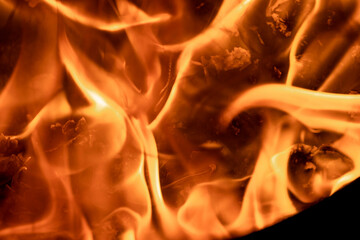 Close-up image of bright orange flames against a backdrop of black ash and burnt debris. A strong visual composition depicting the power, energy, and beauty of nature in the form of the fire element. 
