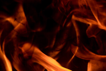 Close-up image of bright orange flames against a backdrop of black ash and burnt debris. A strong...