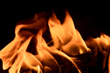 Close-up image of bright orange flames against a backdrop of black ash and burnt debris. A strong visual composition depicting the power, energy, and beauty of nature in the form of the fire element. 