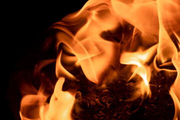 Close-up image of bright orange flames against a backdrop of black ash and burnt debris. A strong visual composition depicting the power, energy, and beauty of nature in the form of the fire element. 