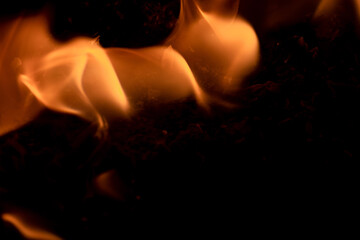 Close-up image of bright orange flames against a backdrop of black ash and burnt debris. A strong visual composition depicting the power, energy, and beauty of nature in the form of the fire element. 