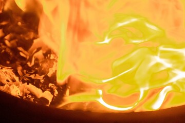 Close-up image of bright orange flames against a backdrop of black ash and burnt debris. A strong...