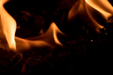 Close-up image of bright orange flames against a backdrop of black ash and burnt debris. A strong visual composition depicting the power, energy, and beauty of nature in the form of the fire element. 