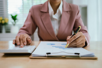A close-up shows hands reviewing financial charts and documents on a clipboard, suggesting detailed office work or analysis.