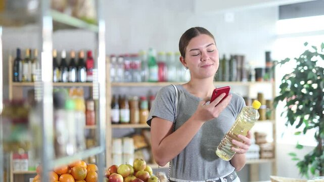 Girl in store scan QR code and study oil assortment. With help of mobile app, buyer receive information about vegetable oil product. She check manufacturer data in registry database of national agency