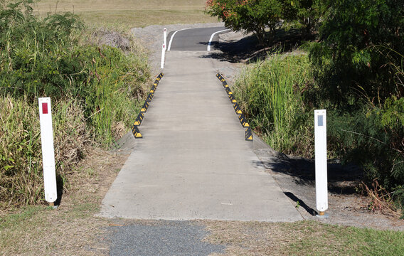 Concrete path over an overgrown creek with two white posts with reflective markers