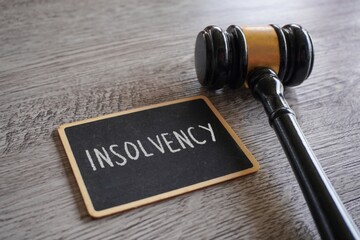 A judge's gavel and a chalkboard with text INSOLVENCY. Legal proceedings, financial regulations,...
