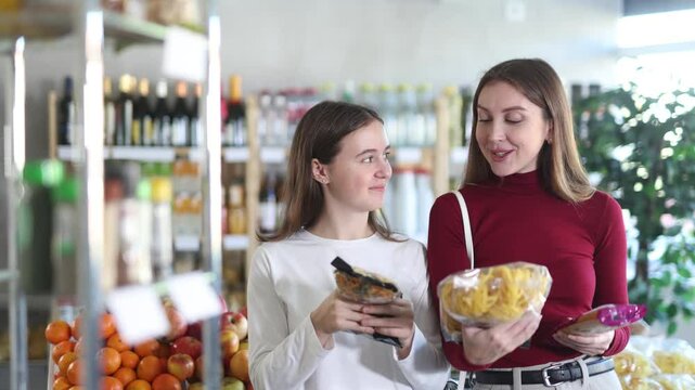 Mom and daughter teen choosing Italian pasta and spaghetti while standing next to grocery shelves in a supermarket. European family chooses pasta to cook at home