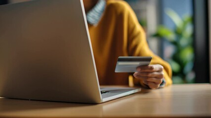 Woman using a laptop to pay with a credit card, during daytime, while sitting at a desk