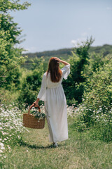 Woman meadow flowers: Redhead in dress walks in a summer meadow carrying basket with daisies.