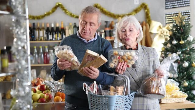 Portrait of happy elderly couple with sweet products in supermarket - nougat, panettone, marzipan, panellets. High quality 4k footage