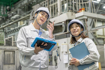 タブレットを持って工場機械を点検する男女作業員