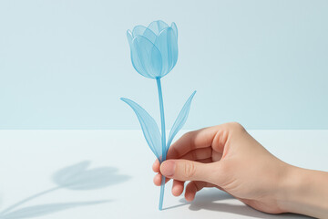 Delicate hand holding translucent blue artificial tulip flower on pastel background symbolizing modern minimal nature inspired decor