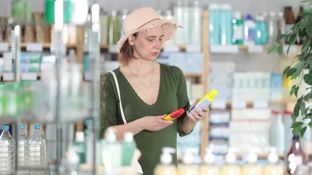 Adult woman in straw hat choosing insect repellent in pharmacy. Buying mosquito sprays. High quality 4k footage