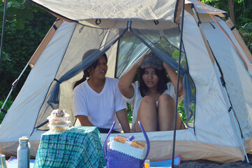 Two teenage girls sit inside a tent on the beach, one wearing a sunhat and gazing outward, enjoying...