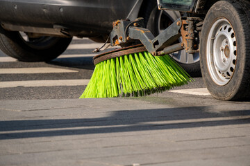 Street sweeper machine actively cleaning road surface with rotating brushes. Bright green bristles...