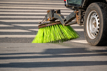 Street sweeper machine actively cleaning road surface with rotating brushes. Bright green bristles efficiently removing debris from pavement in urban setting, enhancing cleanliness and safety.