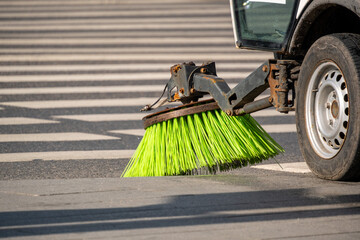 Street sweeper machine actively cleaning road surface with rotating brushes. Bright green bristles efficiently removing debris from pavement in urban setting, enhancing cleanliness and safety.