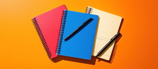Colorful Notebooks and Pens on Orange Background, Back to School Supplies Still Life