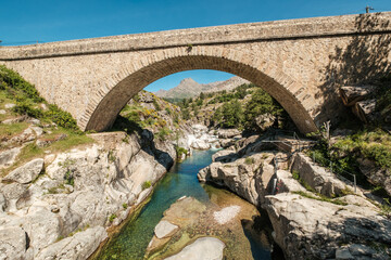 The Ponte Altu bridge at Albertacce on the Mediterranean island of Corsica passing over the crystal clear Golo river with Monte Albanu in the distance