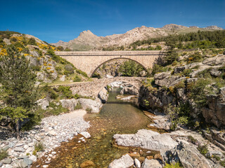The Ponte Altu bridge sits alongside an ancient genoise bridge at Albertacce on the Mediterranean island of Corsica passing over the crystal clear Golo river and with Monte Albanu in the distance