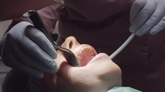 Doctor works on patient widely open mouth using suction tool during procedure. Woman jaw fixed stable allowing clear access for dental treatment