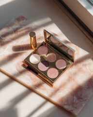 Elegant makeup flat lay featuring pastel eyeshadow palette with variety of shades, beautifully arranged on marble surface, capturing soft natural light and shadows