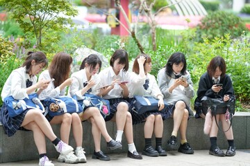 In early summer in Shanghai, near The Bund, Japanese high school girls in uniforms sit at a street corner, chatting and laughing, their smiles adding a touch of youth to the vibrant city atmosphere.