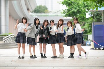 Fototapeta premium In early summer in Shanghai, near The Bund, Japanese high school girls in uniforms stand on a city street, posing for a commemorative photo, their smiles adding charm to the vibrant urban scene.