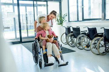 Female doctor pushing wheelchair with mother and son after treatment