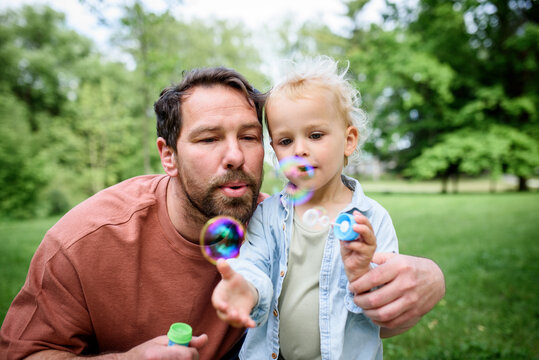 Father and son blowing soap bubbles in park.
