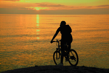 black silhouette of Young one alone male person man standing on hill horizon line with cycle...