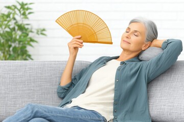 A senior woman using a wooden folding fan and lies on a couch