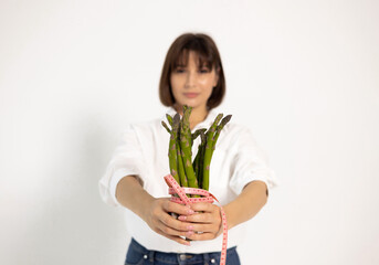 Woman with salad bowl isolated on white. Female holding asparagus wrapped in measuring tape, taking...