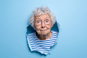 Old lady breaking through blue paper, Funny and expressive senior face, Bright and humorous creative concept image
